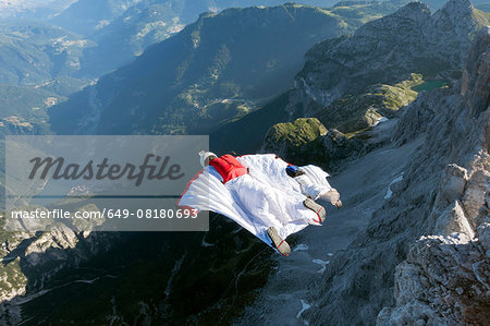 Two male BASE jumpers wingsuit flying from mountain, Dolomites, Italy