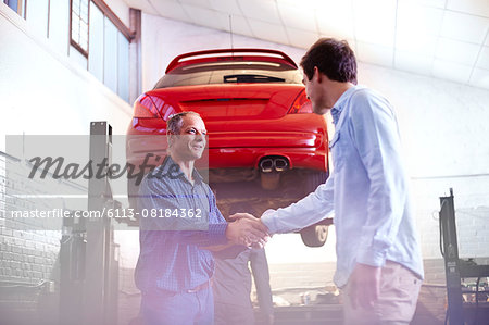 Mechanic and customer handshaking in auto repair shop Mechanic and customer handshaking in auto repair shop
