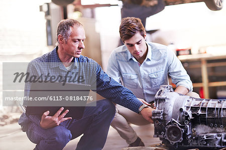 Mechanic with laptop and customer examining engine in auto repair shop Mechanic with laptop and customer examining engine in auto repair shop