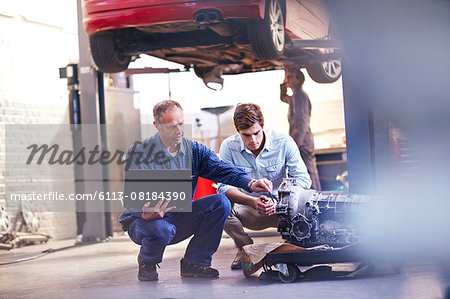 Mechanic and customer with laptop examining engine in auto repair shop