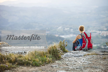 Woman tourist sitting on edge of rock and looking at valley below