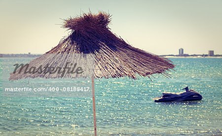 Straw beach umbrella on a background of the cloudless sky and calm sea on a bright sunny day. Toned image. Shallow depth of field.