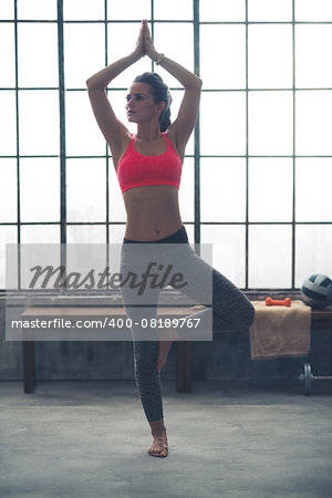 A woman doing the tree pose in a city loft gym is perfectly balanced and calm.