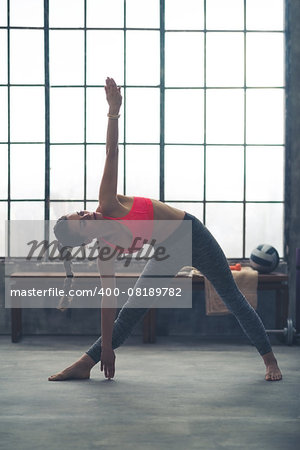A strong, muscular woman is doing the extended triangle pose in yoga in a city loft gym.