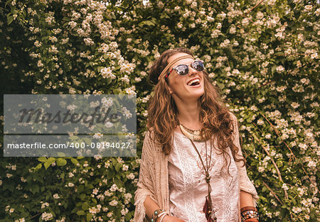 Longhaired hippy-looking young lady in knitted shawl and white blouse standing among flowers and looking up on copy space
