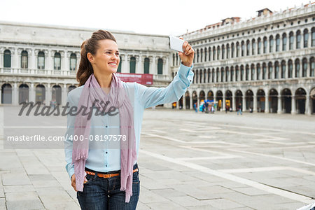 A relaxed, elegant woman tourist holds her device up to take a photo while on St. Mark's Square