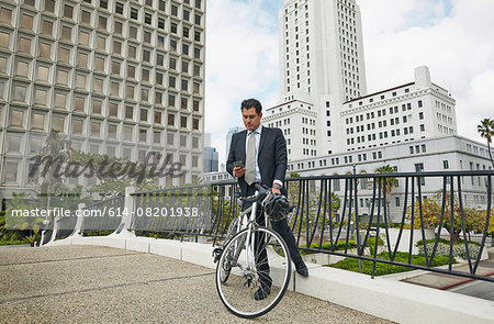 Business man on elevated walkway with bicycle looking at smartphone, Los Angeles City Hall, California, USA