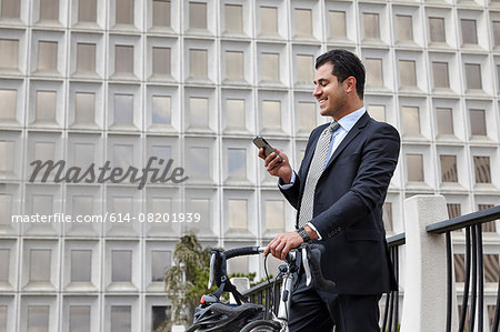 Mid adult business man holding bicycle, looking at smartphone, smiling