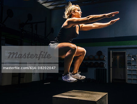 Young woman jumping mid air on gym box with arms reaching out