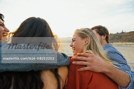 Group of friends sitting together on beach, at sunset, rear view