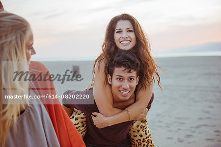 Friends on beach, young man carrying young woman on back