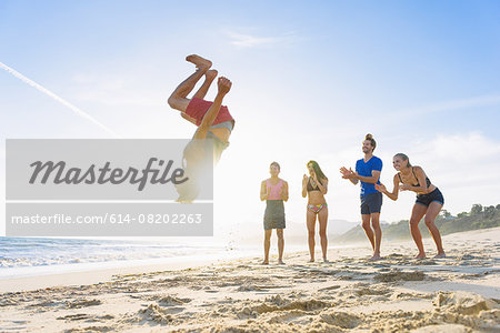 Group of friends on beach watching friend do somersault