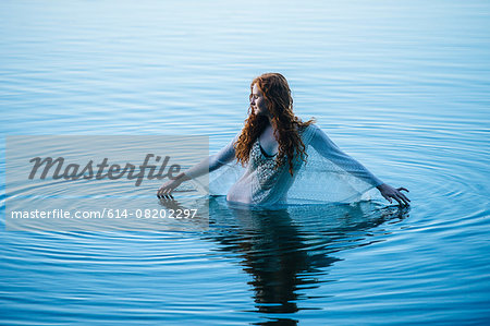 Young woman standing in blue lake rippling surface with her fingers