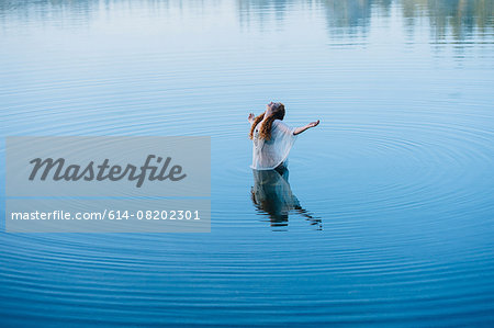 Young woman standing in middle of lake ripples with arms open and head back