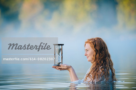 Young woman standing in misty lake gazing at hourglass