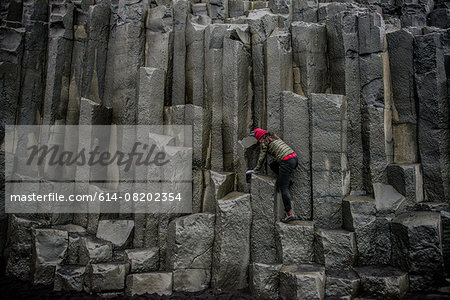 Female tourist climbing up rock formation,  Reynisfjara, Iceland