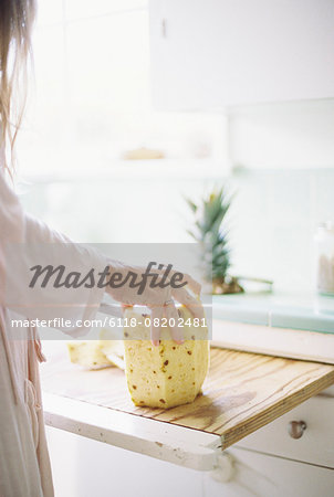 Woman standing in a kitchen, cutting a fresh pineapple.