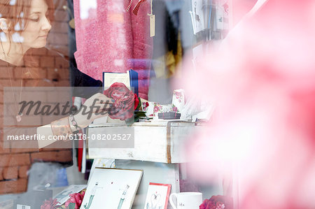A mature woman rearranging the window display of a gift and craft store.