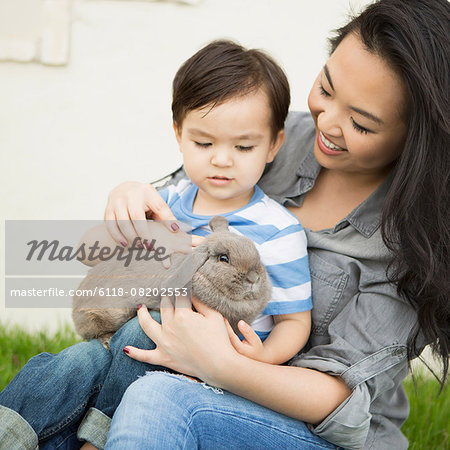 Smiling woman holding a rabbit, her young son sitting on her lap, stroking the animal.