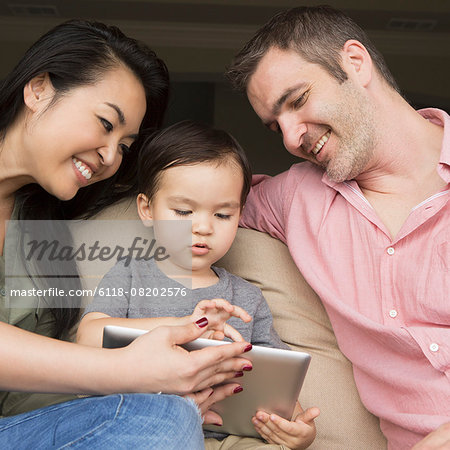 Parents sitting on a sofa with their young son, looking at a digital tablet.