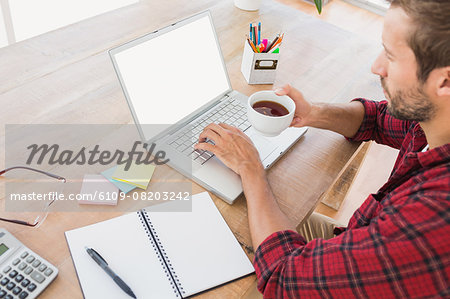 Creative businessman typing on laptop and holding hot beverage