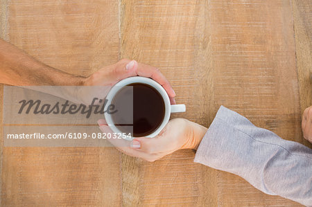 Two hands holding a cup of coffee on wooden table Two hands holding a cup of coffee on wooden table