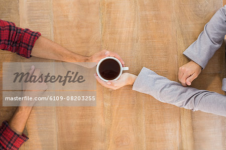 Two hands holding a cup of coffee on wooden table