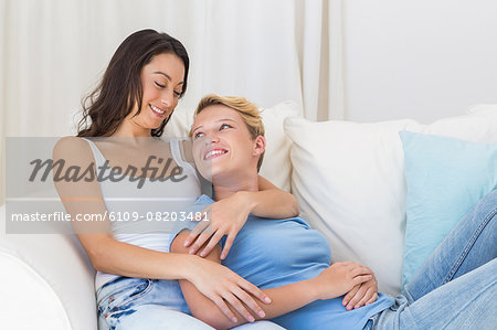 Smiling homosexual couple sitting on couch embracing and looking at each other