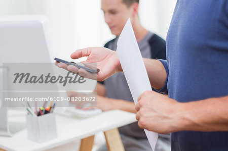 Casual businessman using smartphone with his colleagues behind