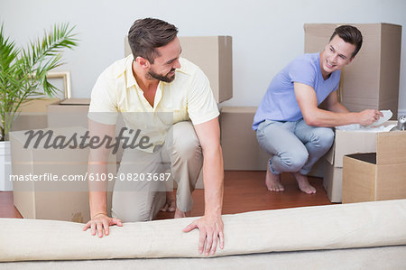 Handsome man unrolling carpet with his boyfriend behind