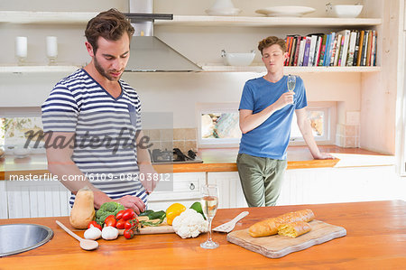 Handsome man cutting vegetables in the kitchen with boyfriend behind