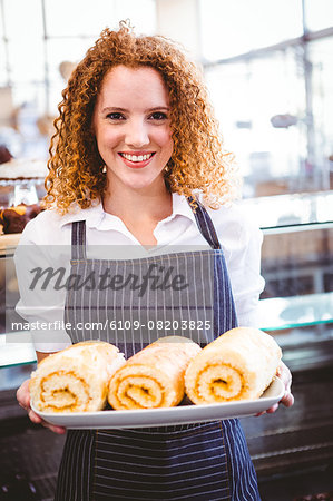 Pretty barista holding plate of Swiss rolls