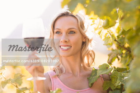 Smiling woman looking at wineglass standing next to grapevine