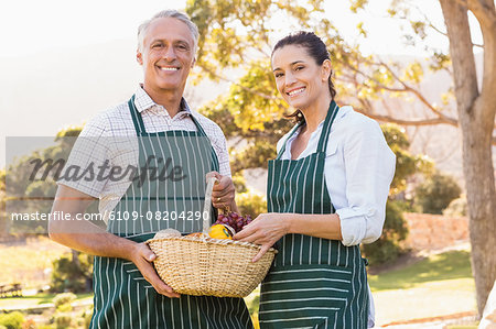 Two mature happy farmers holding a basket of vegetables