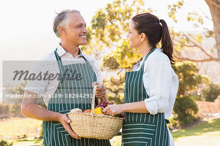 Two mature happy farmers holding a basket of vegetables