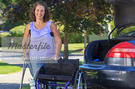 Woman with Spina Bifida standing on crutches near wheelchair and car