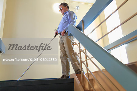 Man with congenital blindness using his cane to go down a stairwell
