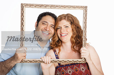 Couple smiling throrugh picture frame against white background