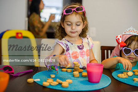 Two young girls sitting at table with drink and cookies