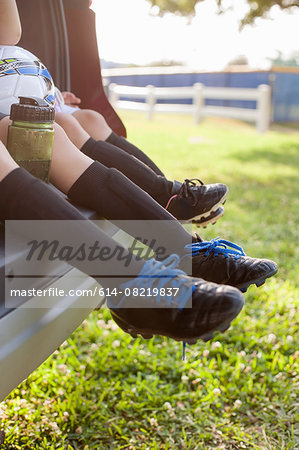 Legs and feet of boy and younger sister sitting in car boot wearing football boots