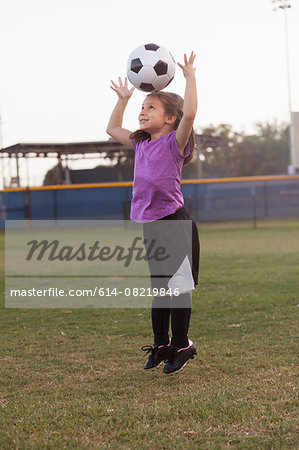 Girl jumping and heading football on practice pitch