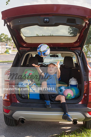 Boy football player sitting in car boot throwing and catching football