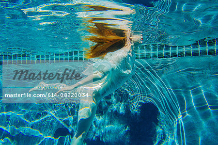 Young woman swimming underwater, wearing thin white shirt