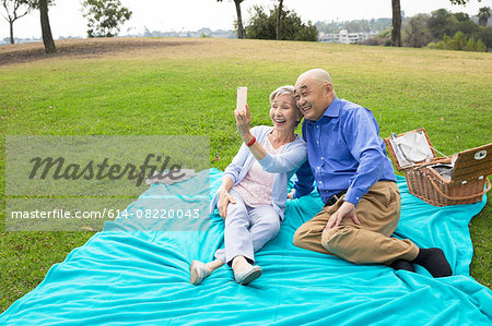 Senior couple having picnic in park, taking self portrait using smartphone