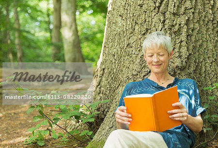 Smiling senior woman reading book against tree in woods
