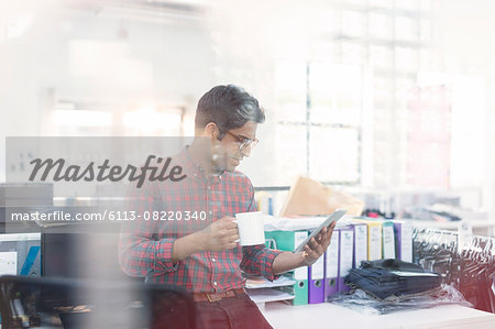 Fashion designer drinking coffee using digital tablet in office