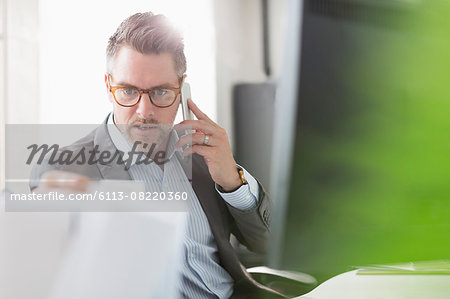 Businessman examining paperwork talking on cell phone in office