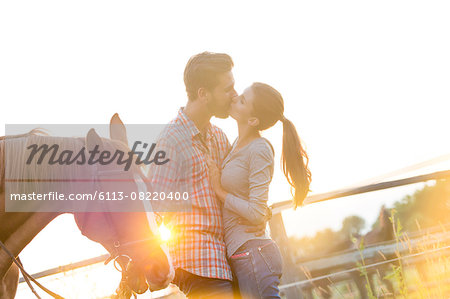 Affectionate couple kissing next to horse in sunny rural pasture