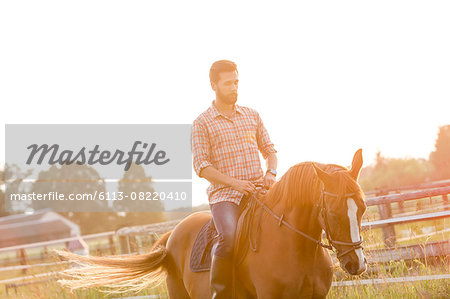 Man horseback riding in sunny rural pasture