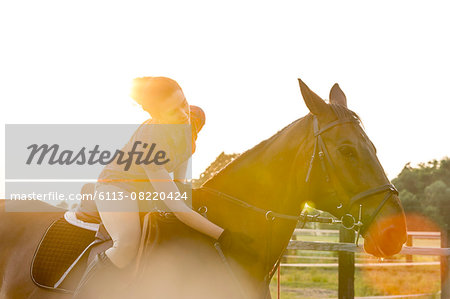 Woman on horseback petting horse in rural pasture